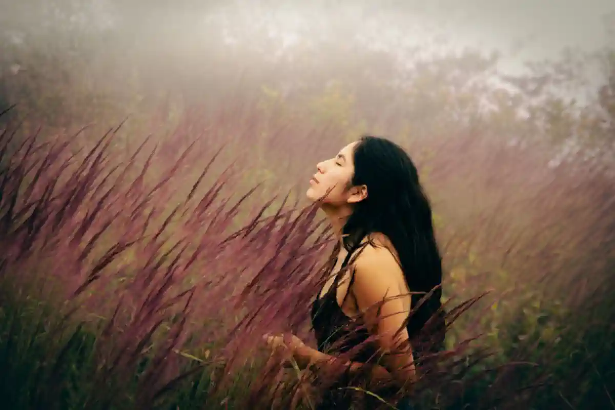 Black haired woman with eyes closed looking up in a foggy filed of check high golden grass