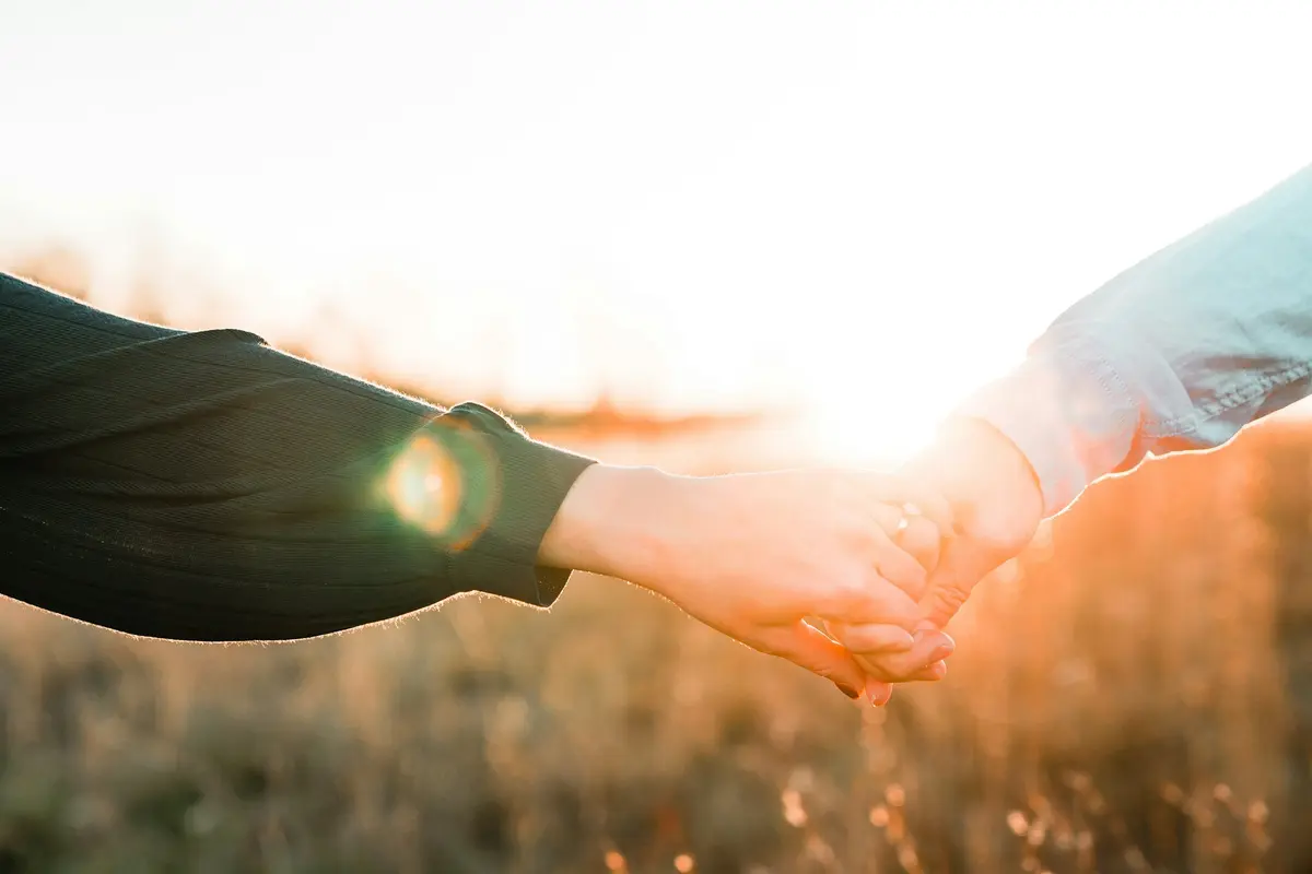 Two people holding hands in a golden field at sunset