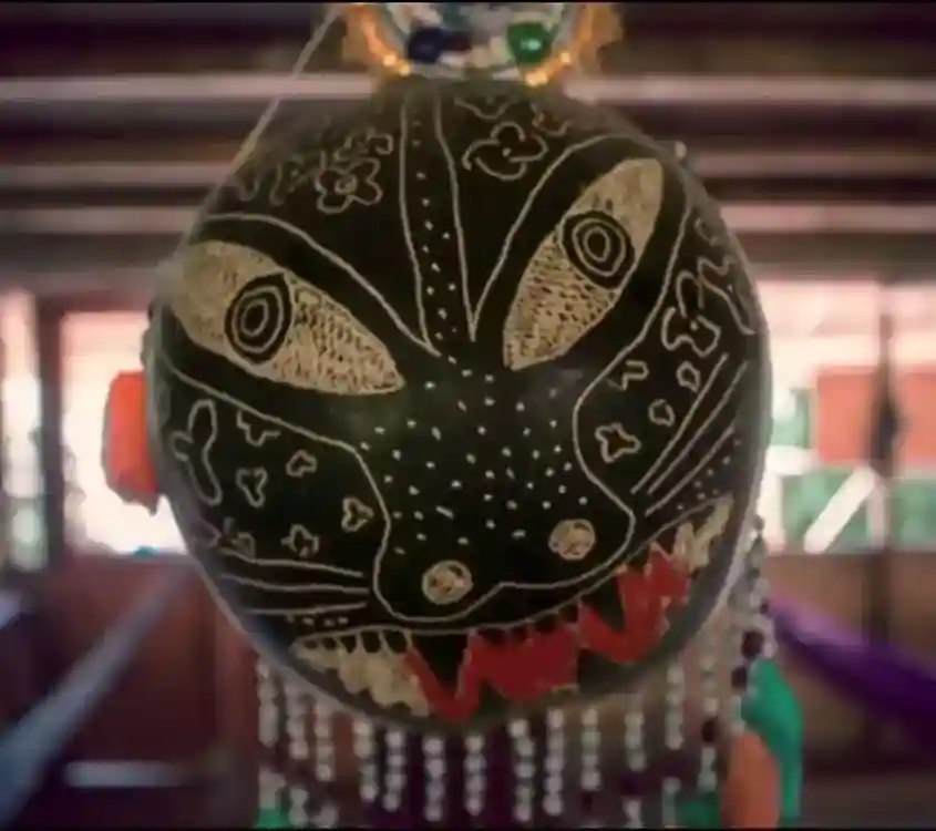 Black mask with large, light-colored eyes, jagged red teeth, and intricate white etched patterns of dots and flowers.