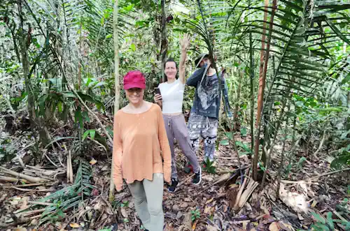 Three women walking in the jungle, one smile at waving at the photographer