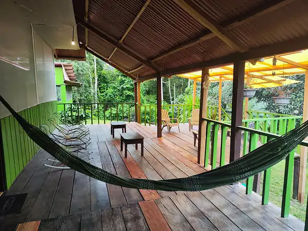 A covered wooden deck with a hammock, wicker chairs and a low table looking out over the jungle.