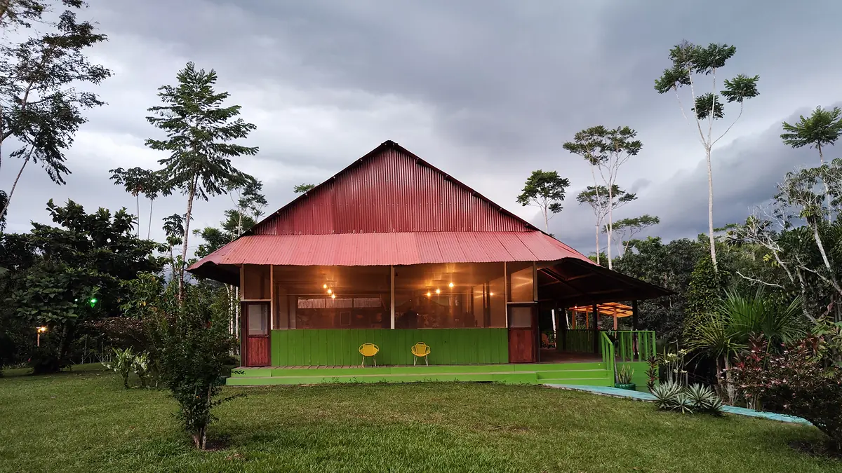 The hall at dusk with its interior lights on and a dark sky above the red roof.