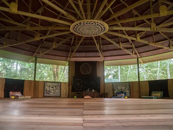 The round maloca interior with its carved ceiling medallion, open wooden floor and altar at the back.