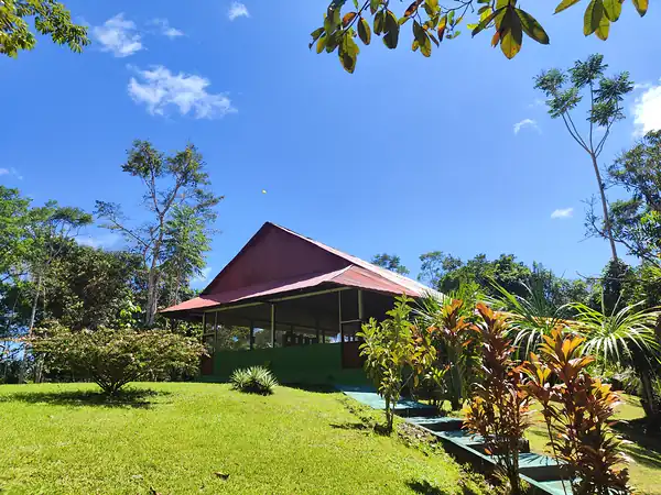 The large open sided hall with a red metal roof, seen across the lawn under a clear blue sky.