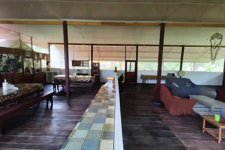 The open-air lodge dining hall with long wooden tables, a tiled centre aisle and lounge sofas at the far end.