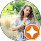 Profile picture Young woman with long brown hair, in a patterned dress, standing in tall golden grass and looking down