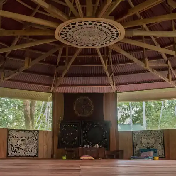 Inside of a moloca ready for an ayahuasca ceremony.  Wooden plank floor, shipibo cloths on walls, view of trees through large screened windows